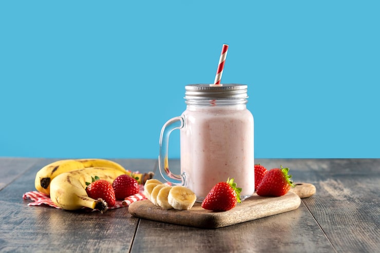 Foto grátis preparando smoothie de morango e banana em pote na mesa de madeira e fundo azul