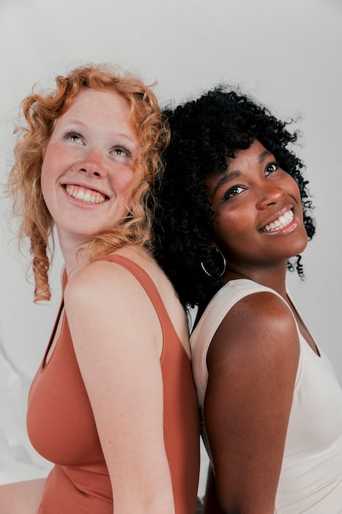 Foto grátis retrato sorridente de uma jovem africana e uma mulher caucasiana sentadas de costas juntas olhando para cima