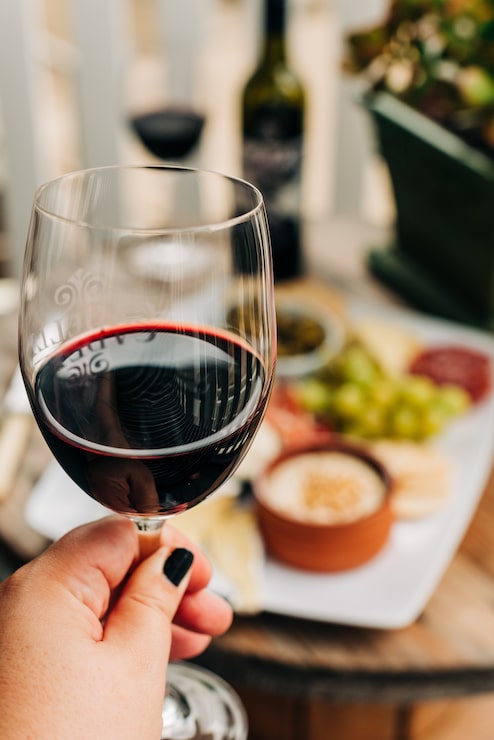 Foto grátis tiro vertical seletivo closeup de uma mulher segurando um copo de vinho cheio de vinho tinto escuro