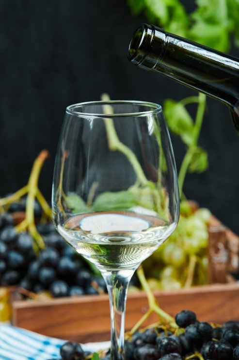 Foto grátis um copo de vinho branco com um cacho de uvas vermelhas.