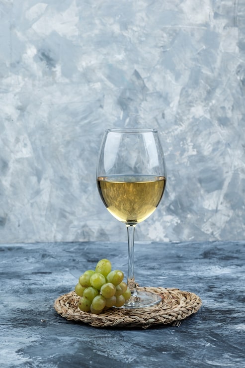 Foto grátis uvas verdes com uma taça de vinho vista lateral em gesso sujo e fundo de roteiro de vime