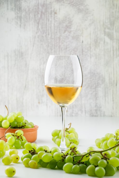 Foto grátis uvas verdes com vinho em copo em uma placa de barro em superfície branca