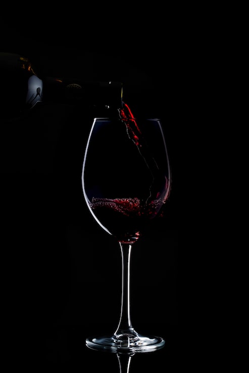 Foto grátis vinho vermelho está sendo derramado em copos com caule longo no escuro
