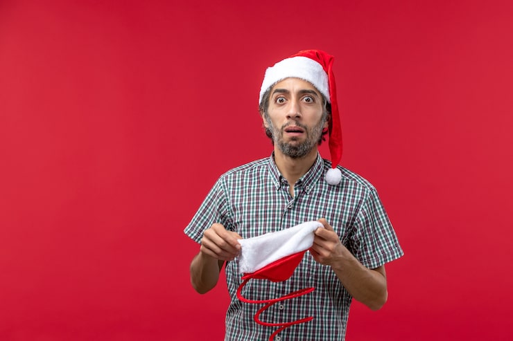 Foto grátis vista frontal de um jovem com boné de brinquedo de natal na parede vermelha