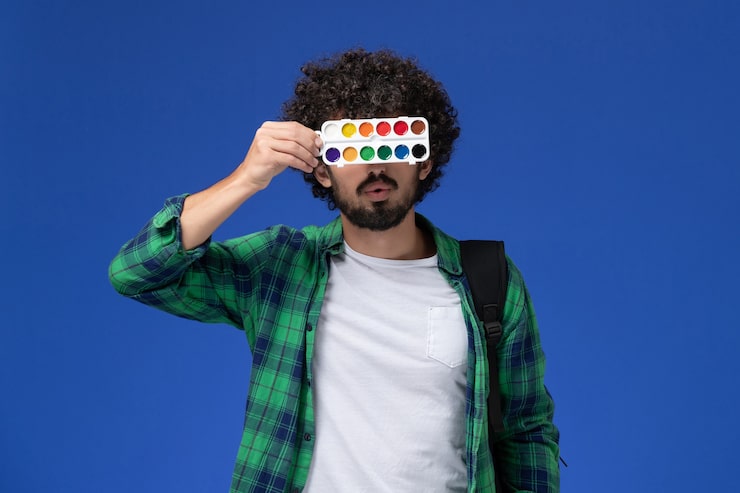 Foto grátis vista frontal do estudante do sexo masculino com camisa xadrez verde e mochila preta segurando tintas para desenho
