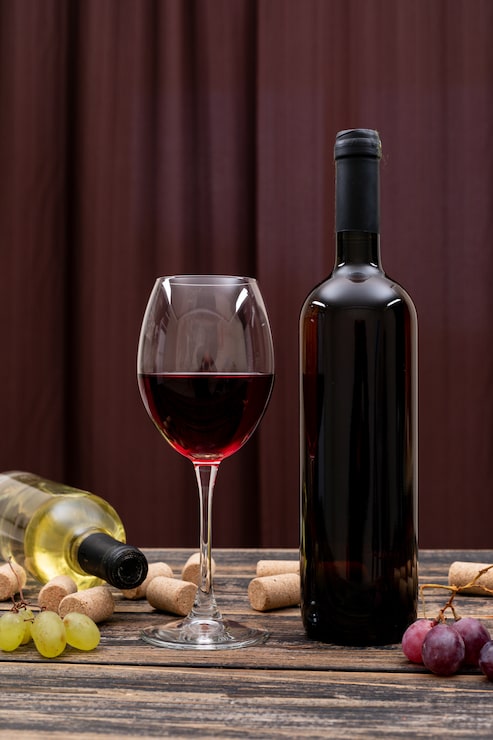 Foto grátis vista lateral vinho tinto em garrafa, copo e uva na mesa escura e vertical