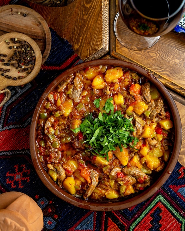 Foto grátis vista superior da carne de boi estufada com batatas pappers verdes e ervas em uma tigela de barro em uma mesa de madeira