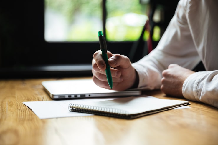Kostenlose Foto beschnittenes foto der hand des mannes, die grünen stift hält, während notizen macht