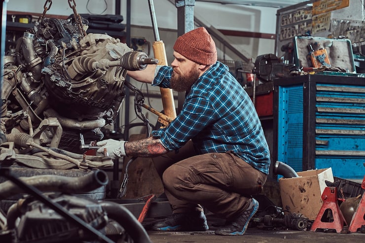 Kostenlose Foto brutaler tätowierter bärtiger mechaniker repariert den automotor, der auf der hydraulischen hebebühne in der garage angehoben wird. tankstelle.