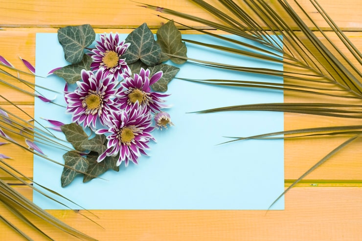 Kostenlose Foto chrysanthemenblume mit efeu- und palmblättern auf leerem papier über dem hölzernen hintergrund