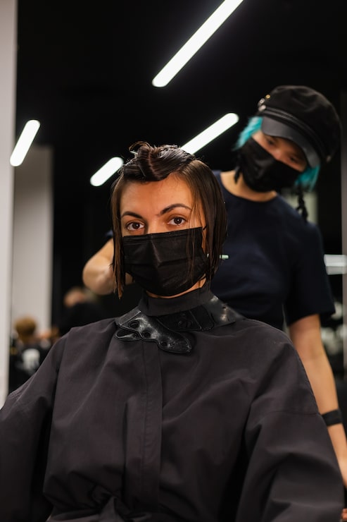 Kostenlose Foto ein professioneller friseur macht einen kundenhaarschnitt. das mädchen sitzt in einer maske in schönheit im salon