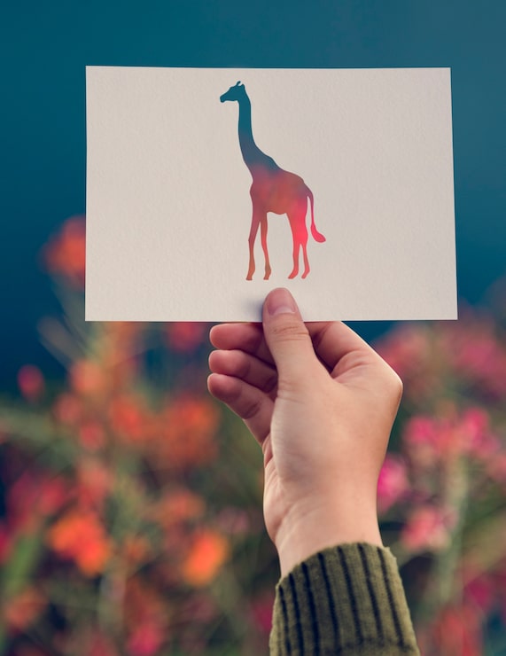 Kostenlose Foto hand halten giraffen-papier, das mit blumen-hintergrund schnitzt