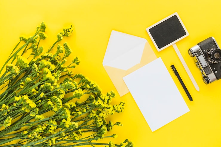 Kostenlose Foto schöner blumenstrauß; karte; briefumschlag; stift; kamera und plakat auf gelbem hintergrund
