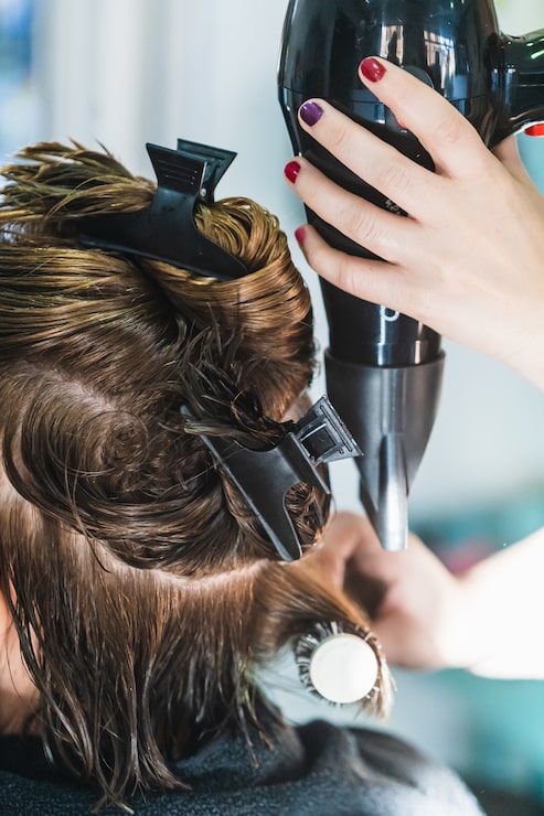 Kostenlose Foto vertikale nahaufnahmeaufnahme eines friseurs, der die kurzen haare einer frau in einem schönheitssalon föhnt