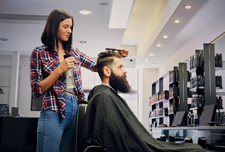 Kostenlose Foto weiblicher friseur, der haare eines bärtigen hipster-männchens in einem salon schneidet.