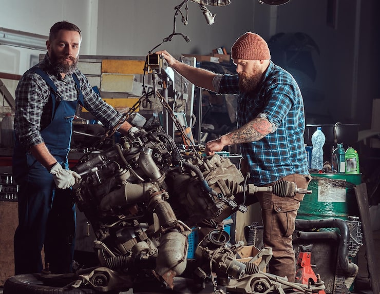 Kostenlose Foto zwei bärtige mechaniker reparieren den automotor, der auf der hydraulischen hebebühne in der garage angehoben wird. tankstelle.