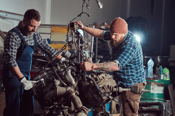 Kostenlose Foto zwei bärtige mechaniker reparieren den automotor, der auf der hydraulischen hebebühne in der garage angehoben wird. tankstelle.