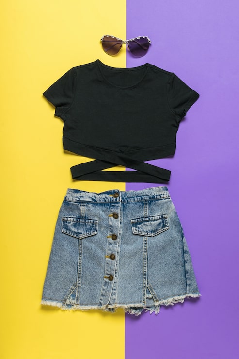 Foto una camiseta negra, gafas negras y una falda de mezclilla sobre una superficie amarilla y morada.
