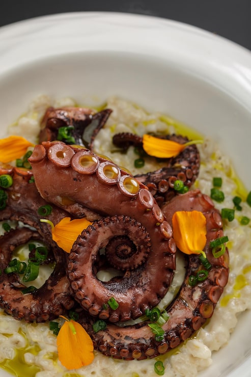Foto cebada perlada con tentáculos de pulpo en un gran plato blanco aislado sobre fondo negro