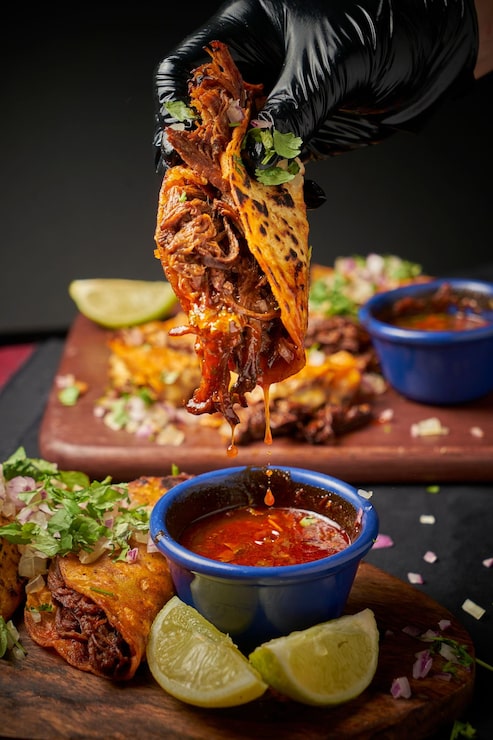 Foto close-up vertical de uma mão mergulhando tacos recém-feitos em molho quente