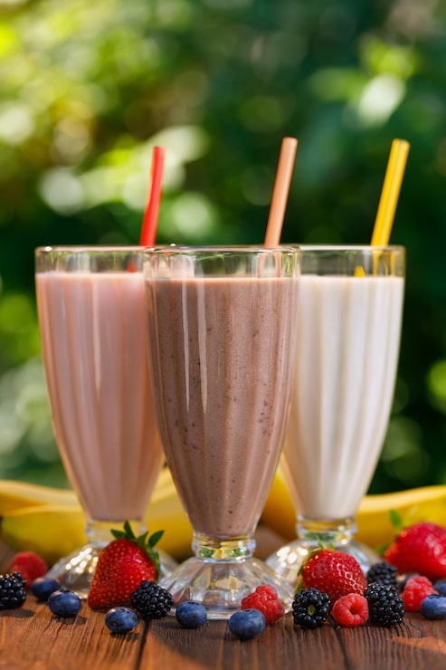Foto conjunto de milkshakes em copos com palha e bananas frescas e bagas na mesa ao ar livre
