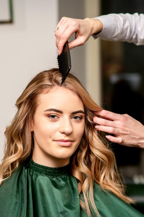 Foto friseur kämmt lange haare einer jungen kaukasischen frau, die in die kamera schaut und im schönheitssalon lächelt