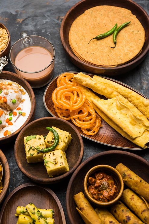 Foto grupo de lanches guzerate como jalebi-fafda, thepla, khaman dhokla, aloo bhujiya, khandvi, khakra, dahi vada, gathiya com chá quente
