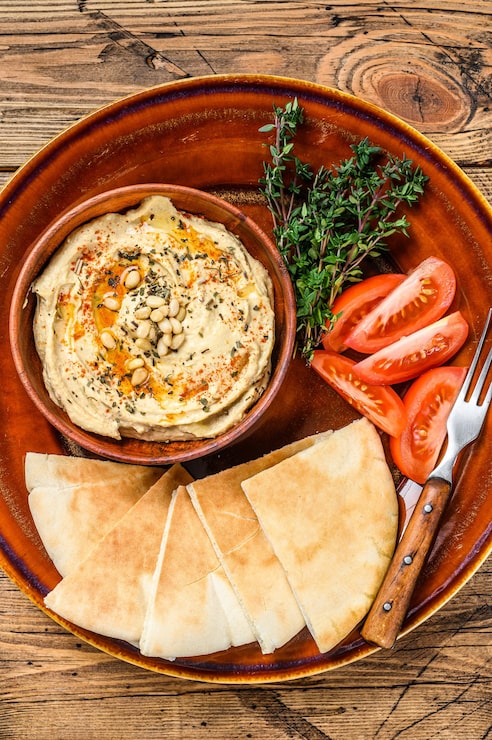Foto hummus fresco com pão pita, tomate e salsa em um prato rústico.