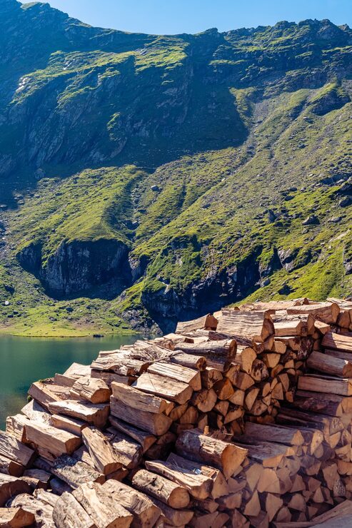 Foto leña apilada con vistas al lago balea y empinadas laderas verdes de montaña en rumanía