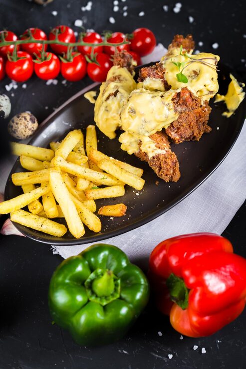 Foto numa travessa jazem coxas de frango fritas em molho de queijo, tomate cereja, batatas fritas, escuras e melancólicas,