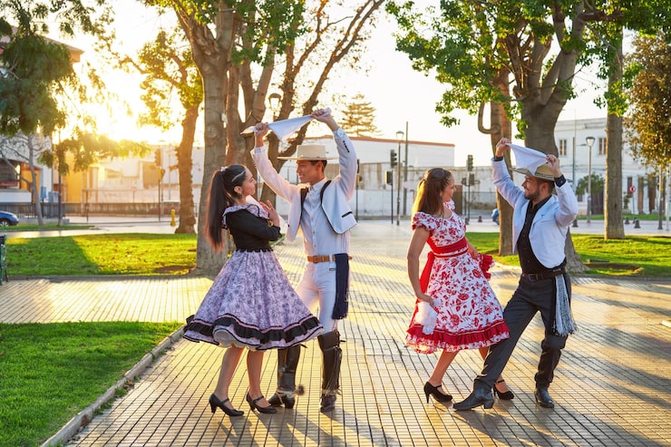 Foto retrato de grupo de cuatro jóvenes latinoamericanos bailando cueca vestidos de huaso en la plaza de la ciudad