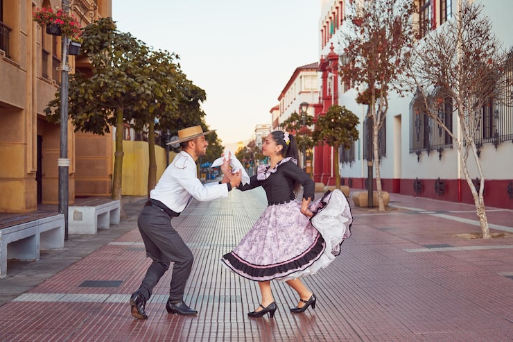 Foto retrato de pareja vestida con ropa tradicional de huaso bailando cueca en la calle de la ciudad