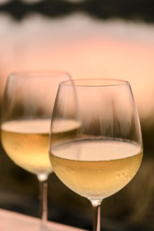 Foto um jantar romântico no verão em uma praia ao pôr do sol com dois copos de vinho branco