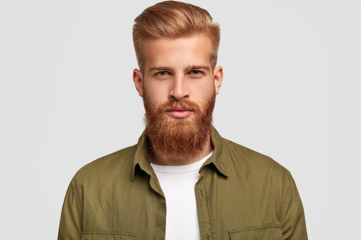 Gratis Foto portrett av attraktiv skjeggete mann med trendy frisyre, har flott tykt skjegg og bart, ser alvorlig ut, lytter oppmerksomt til nyheter fra samtalepartner, isolert over hvit vegg. livsstilskonsept