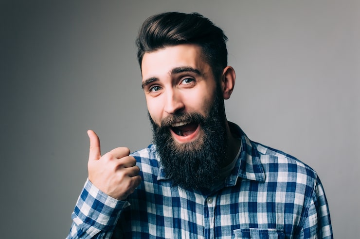 Gratis Foto portrett av en smilende mann i briller som viser tommel opp over grå vegg