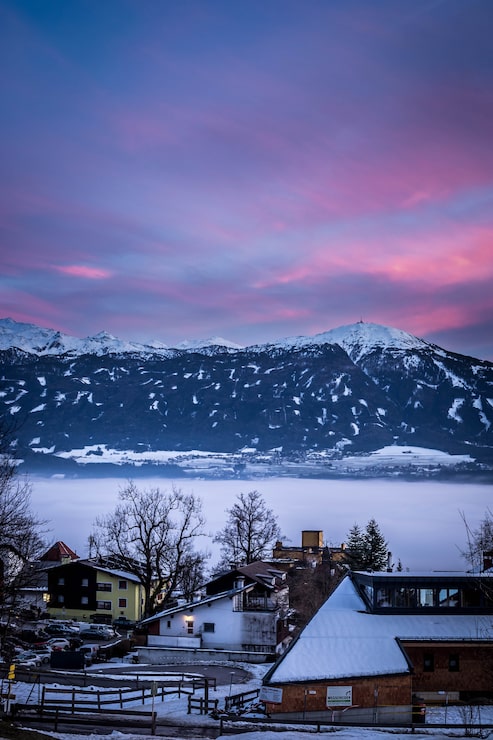 Gratis Foto små snødekte hus i en by med fantastisk himmel og fjell