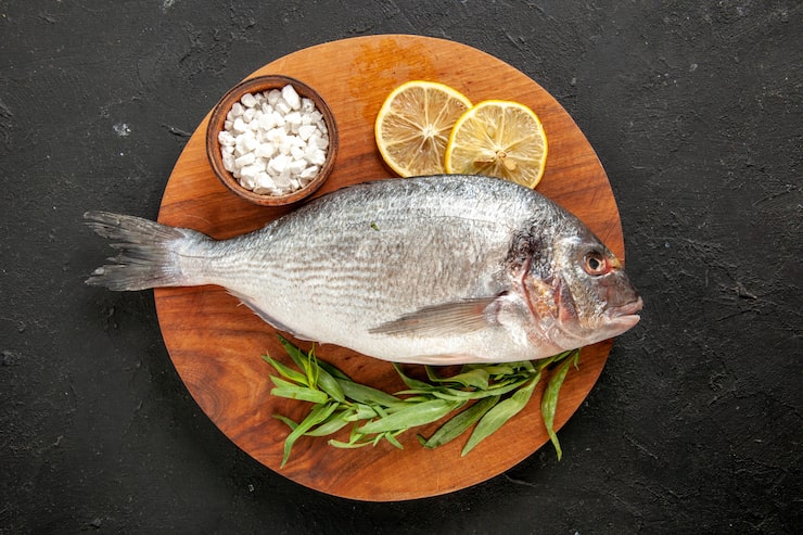 Gratis Foto topputsikt estragon rå sjøfisk havsalt i bolle sitronskiver på rundt trebrett på svart