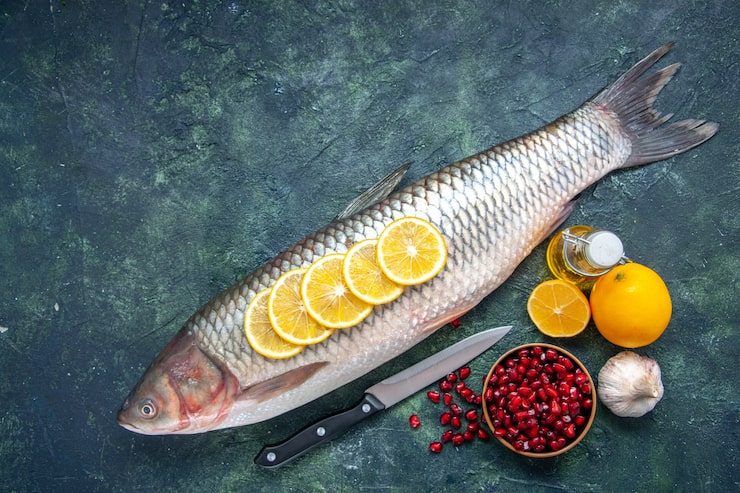 Gratis Foto toppvisning av fersk fisk med sitronskiver, kniv, granateplefrø, bolle på kjøkkenbordet med kopiplass
