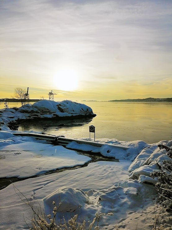 Gratis Foto vertikalt bilde av en øy dekket av snø, omgitt av havet under solnedgangen i norge