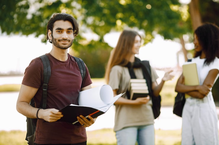 Gratis Bild fokus på en indisk pojke som står separat. grupp av internationella studenter som står tillsammans i parken vid universitetet