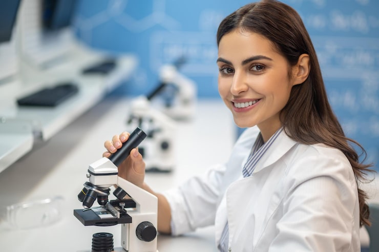 Gratis Bild glad kvinna nära mikroskop som tittar på kameran