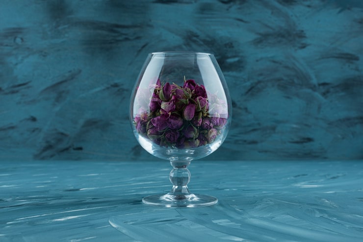 Gratis Foto glas med tørrede lilla roser placeret på blå overflade.