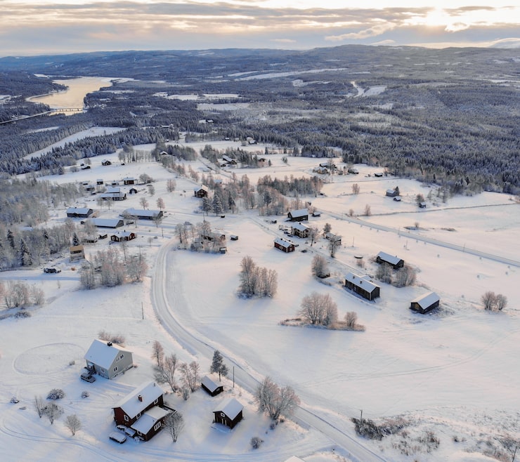 Gratis Bild högvinkelbild av en stad täckt av snö omgiven av skogar och en sjö under en molnig himmel
