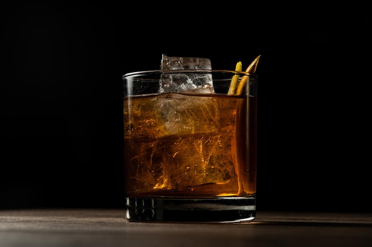 Gratis Bild närbild av ett glas old fashioned-cocktail med is på ett träbord med suddig bakgrund