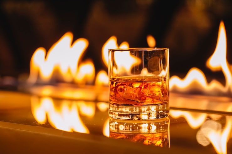 Gratis Bild sido vy av ett glas whisky med is mot en bakgrund av en brinnande flamma