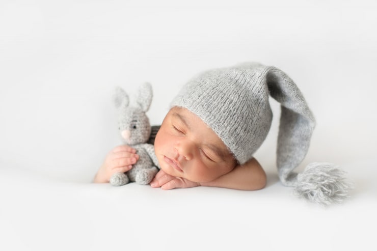 Gratis Foto sød spædbarn, der sover med grå hæklet hat og med legetøjskanin