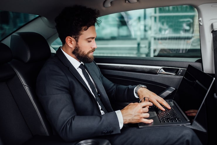 Gratis Bild stilig, skäggig, leende toppchef i svart kostym som arbetar på sin laptop på baksätet av bilen