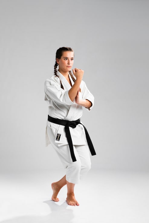 Gratis Bild tjejfighter i stridsposition som bär den vita uniformen på grå bakgrund