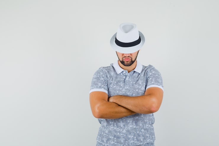 Gratis Bild ung man som står med korsade armar i randig t-shirt och hatt och ser seriös ut. framifrånvy.