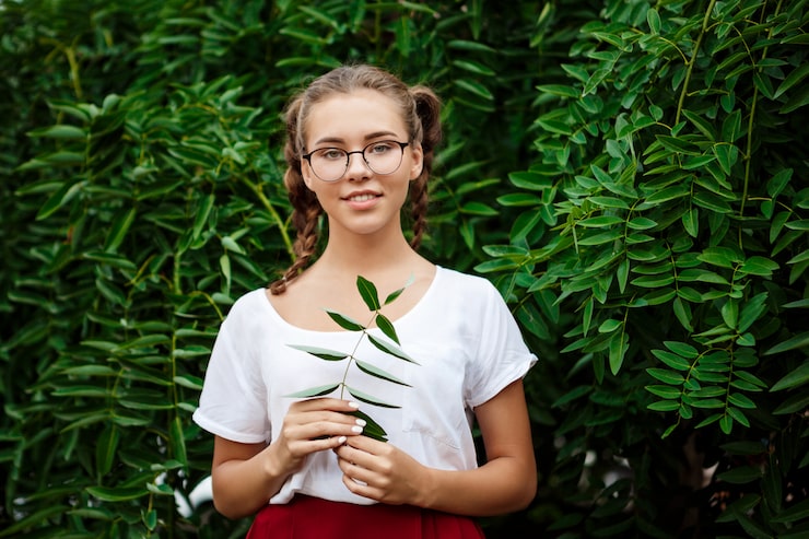 Gratis Bild ung vacker kvinnlig student i glasögon som ler och poserar över löv utomhus.